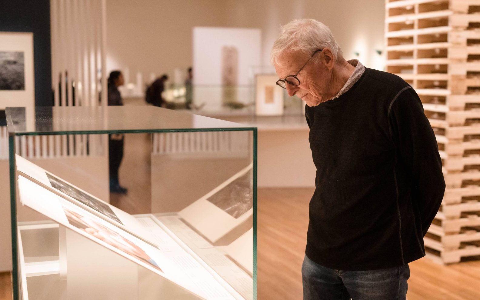 Older man studying artwork in a display case in the Aga Khan Museum gallery with his hands behind his back