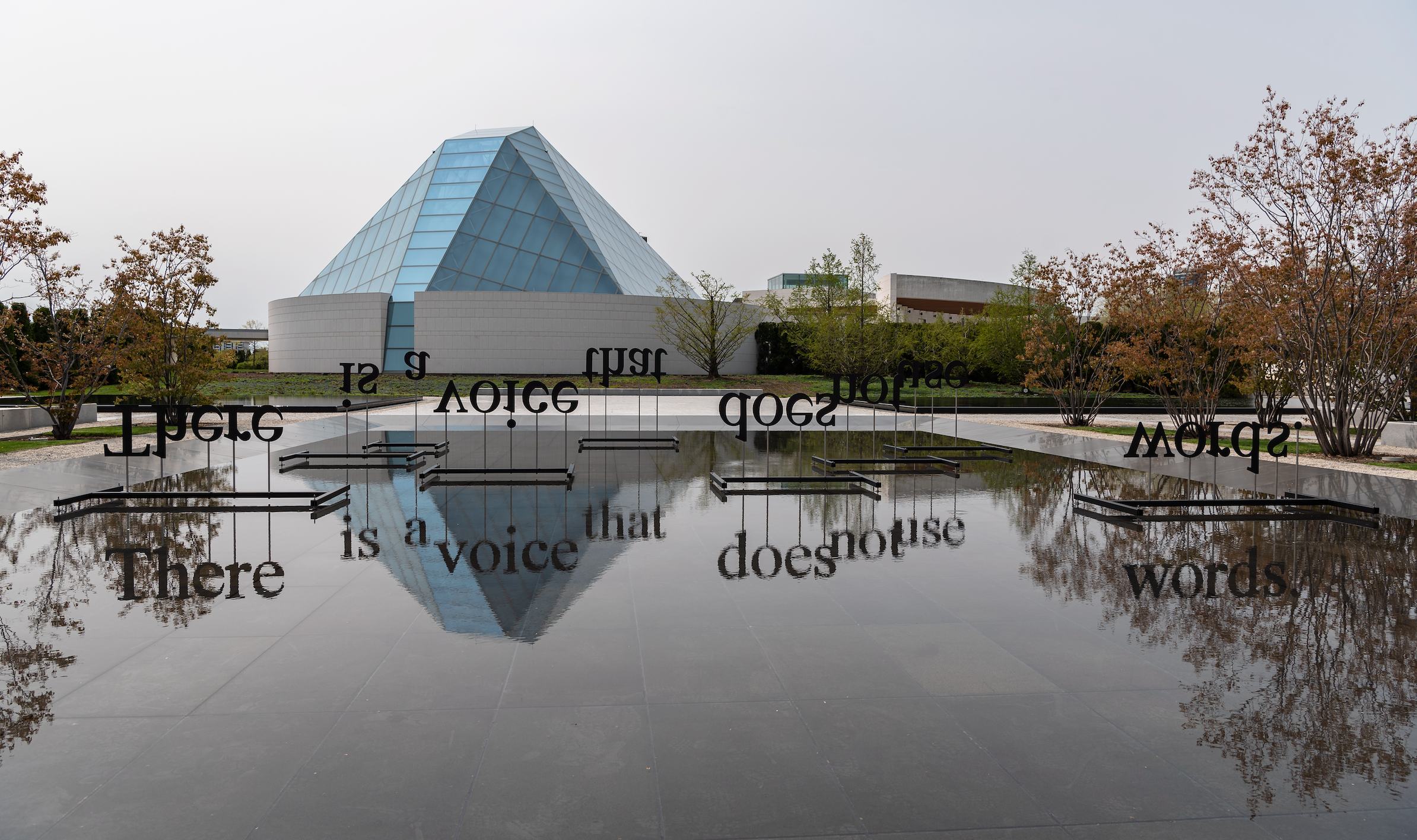 Word artwork displayed in one of the reflective pools at the Aga Khan Park with the Ismaili Centre, Toronto in the background
