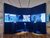 One side of an interactive installation consisting of a blue wall with three TV screens showing videoclips of elephants and in front of the screens there are three mounts with with items representing body parts of elephants and each mount has an button that plays an elephant sound