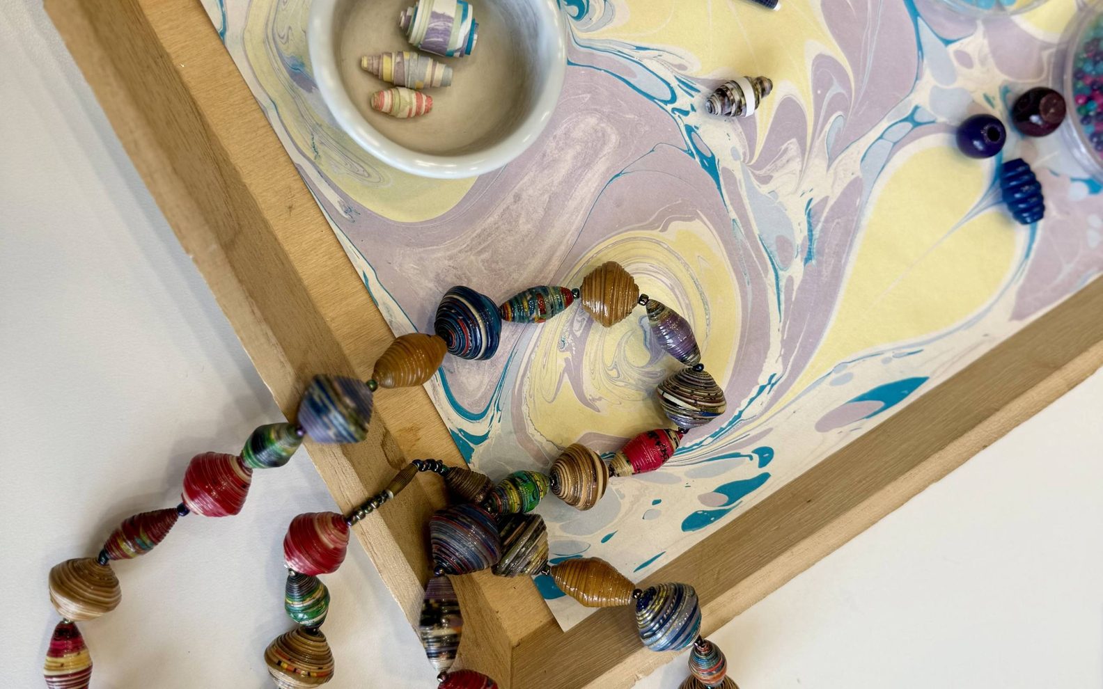 a paper bead necklace draped on a tray with individual beads and supplies around it.