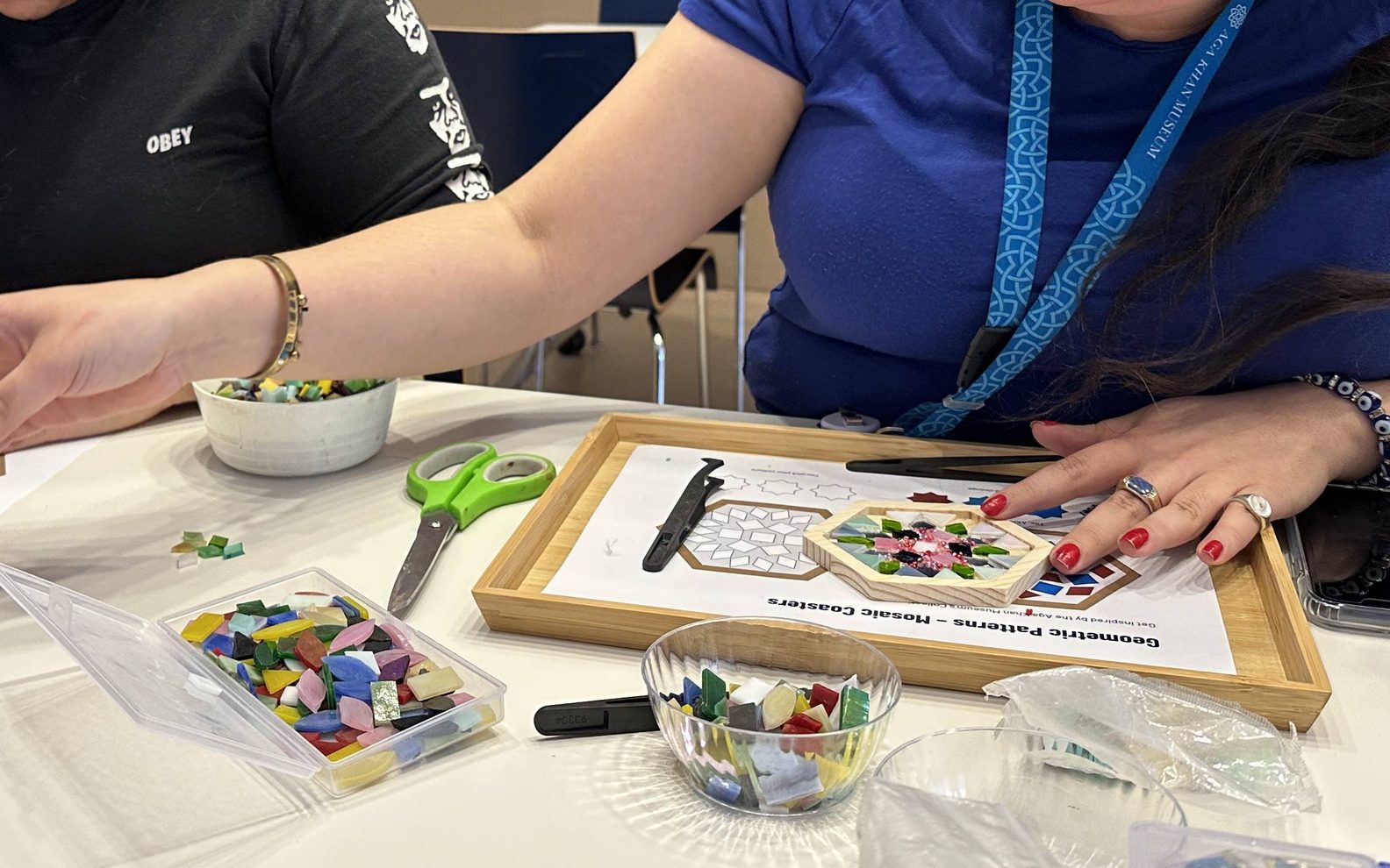 Two adults creating mosaic tiles using glue and glass pieces.