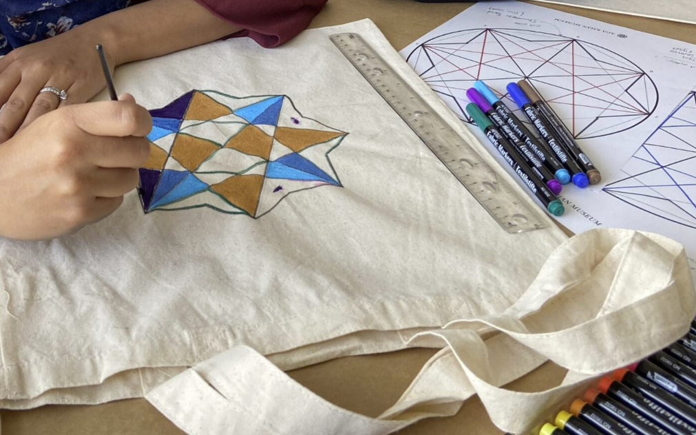 An adult painting a pattern on a canvas tote bag.