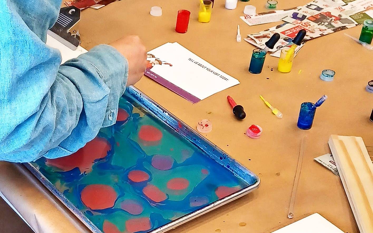 A close up of an adult from the back dropping paint in a tray filled with water and colour for water marbling.