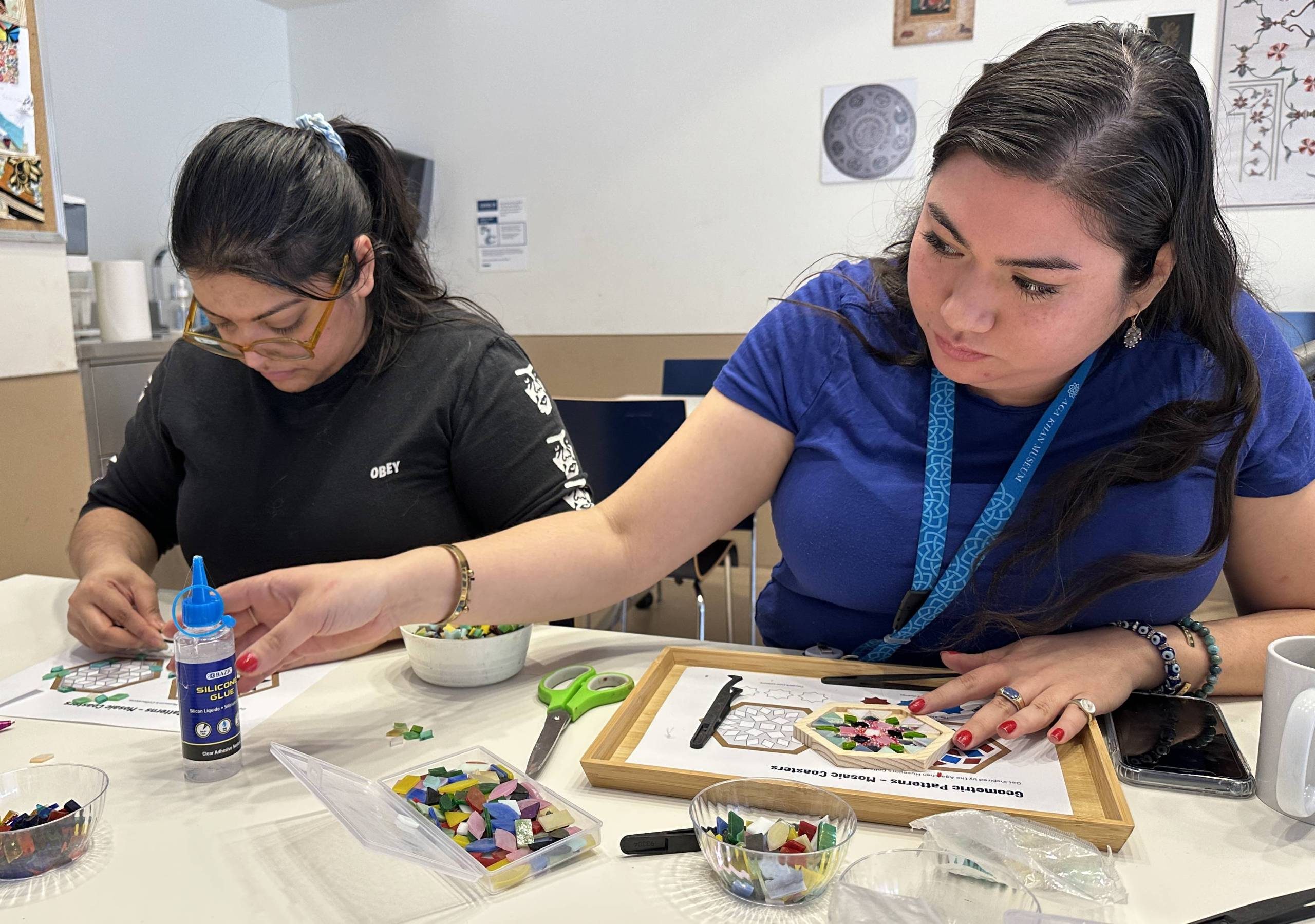 Two adults creating mosaic tiles using glue and glass pieces.